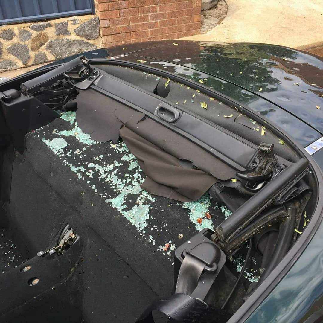 Shattered glass and torn fabric on the back seat area of a convertible car with damaged soft top.