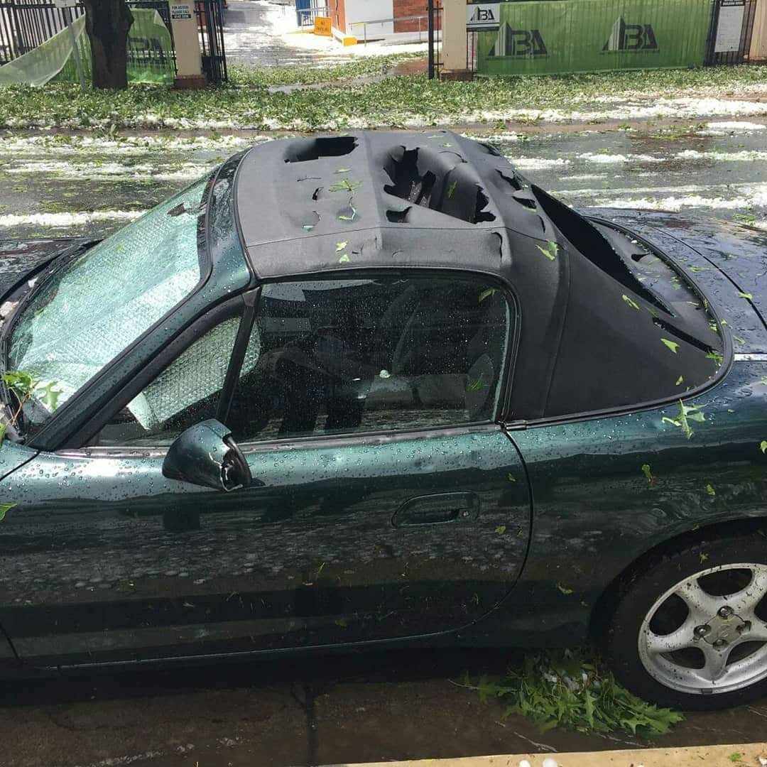Green convertible car with a severely torn soft top roof, parked on a wet street with debris.