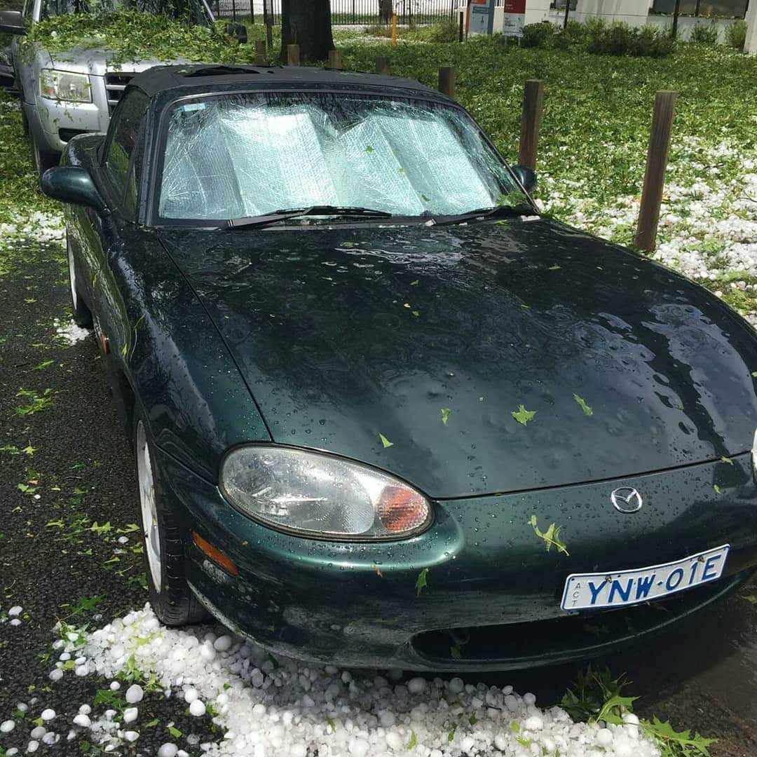 Green Mazda car parked outside with hailstones, leaves, and a sunshade inside the windshield.