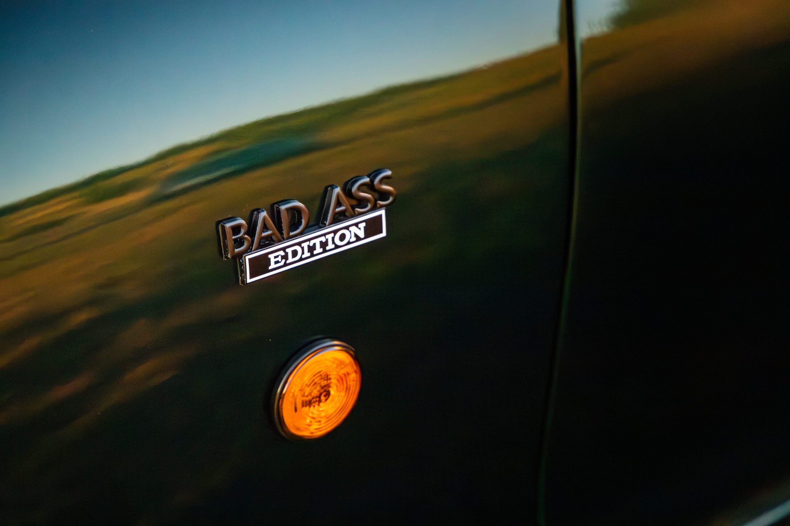Close-up of a black vehicle with a "BAD ASS EDITION" badge and an orange reflector below it.