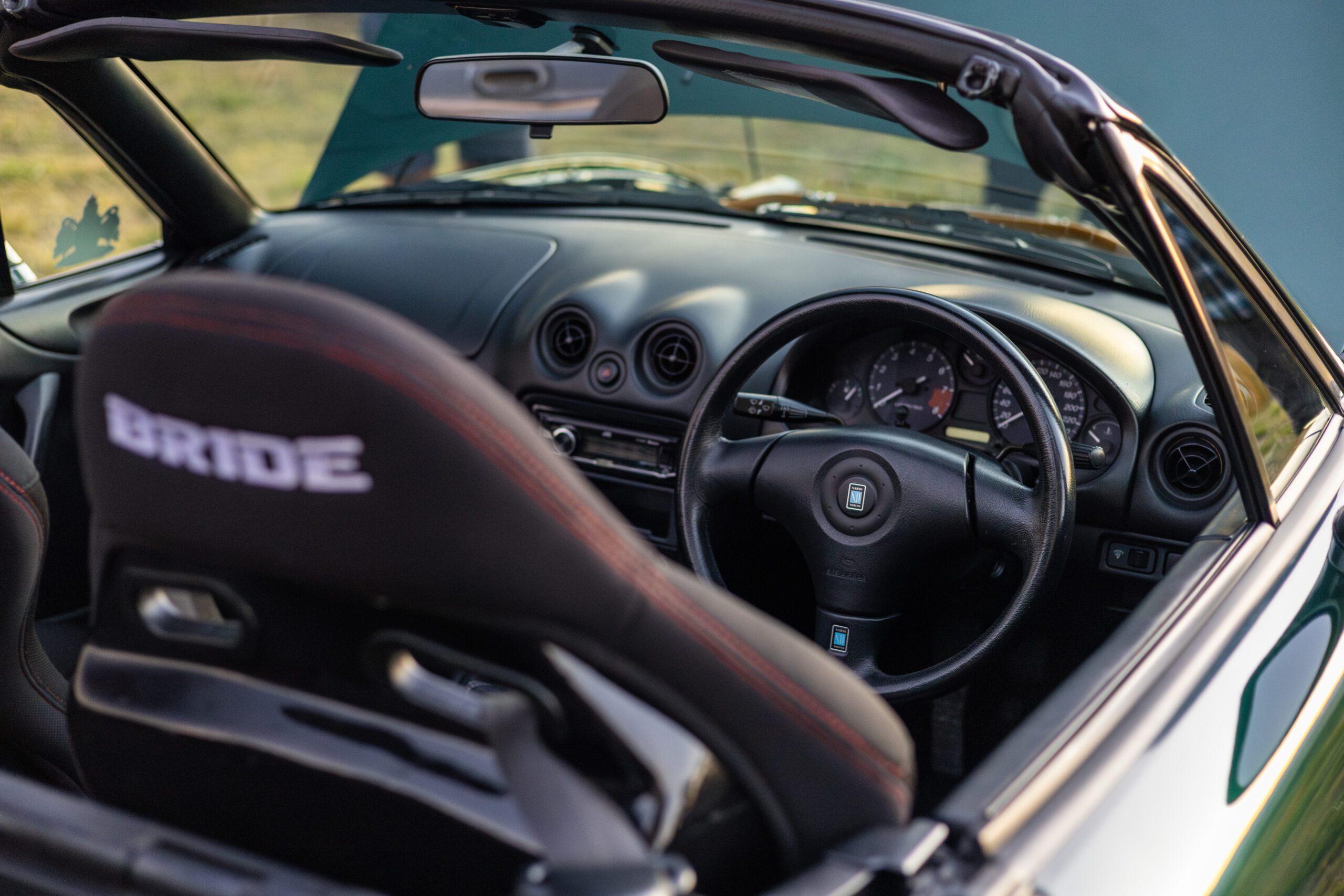 Interior view of a convertible sports car showing a Bride racing seat and a right-hand steering wheel.