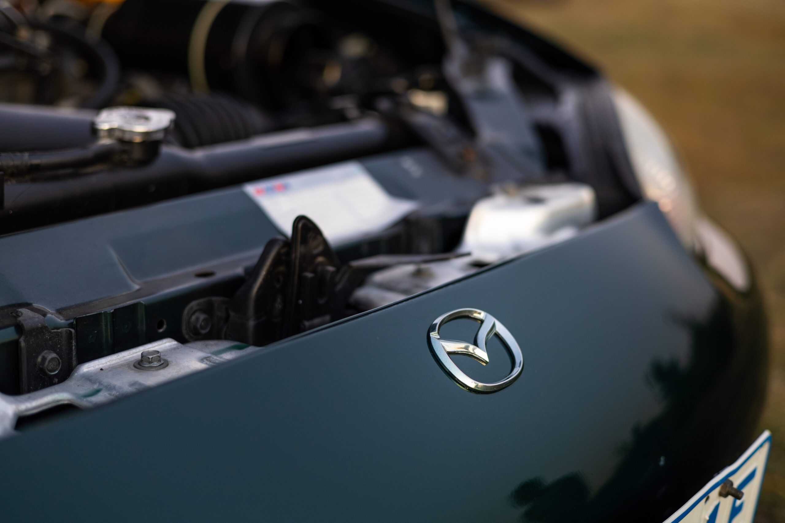 Close-up of a green car hood with a Mazda logo and part of the engine visible in the background.
