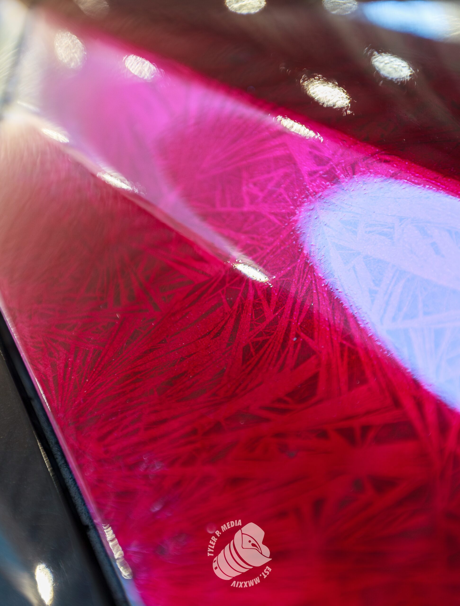 Close-up of a red, glossy surface with intricate etched patterns and light reflections.