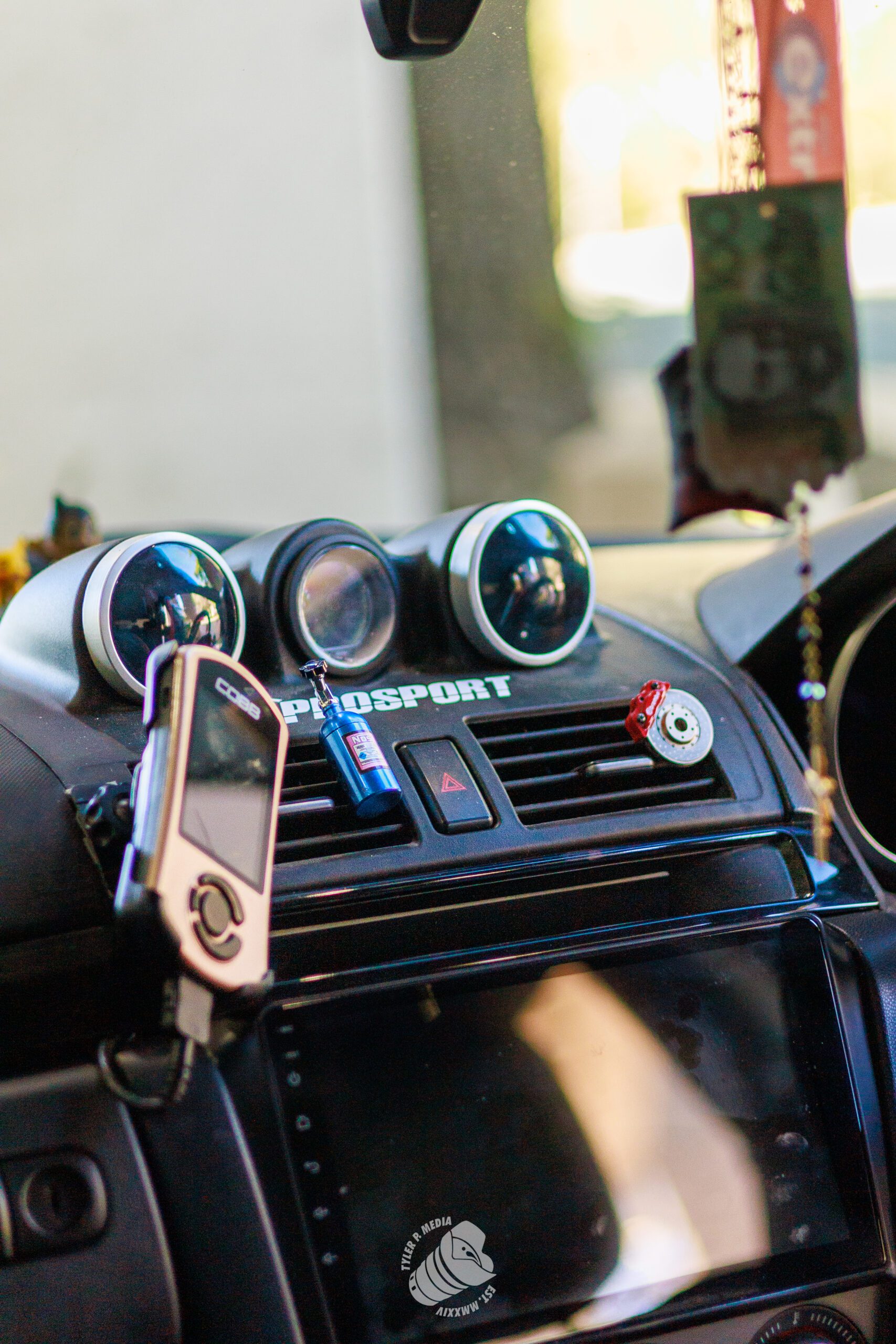 Close-up of a car dashboard with ProSport gauges, a COBB device, and small decorative items on the air vent.