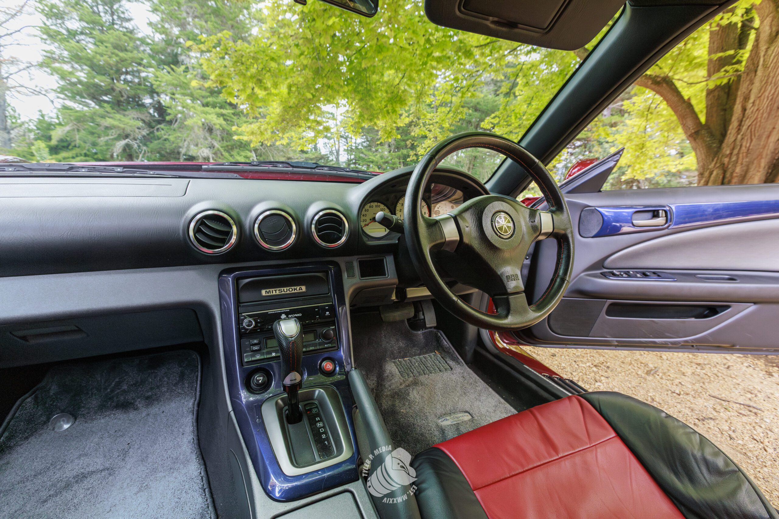 Interior of a right-hand drive Mitsuoka car with black and red leather seats and open door.