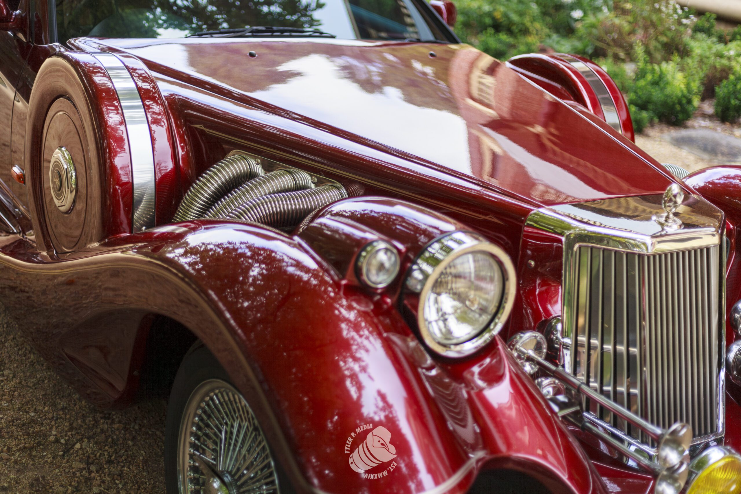 Close-up of a shiny vintage red car front with chrome grille, round headlights, and side exhaust pipes.