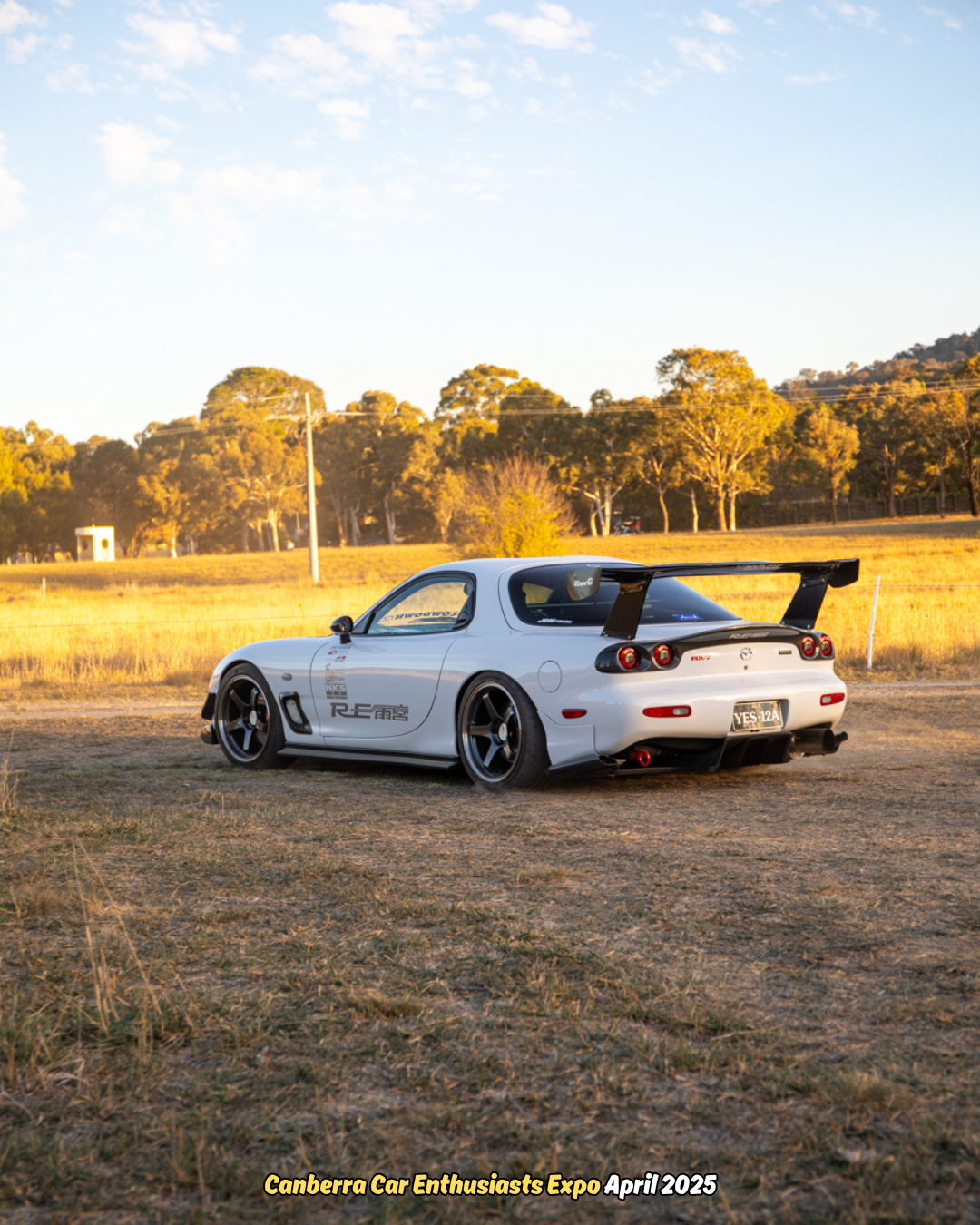 White Mazda RX-7 sports car with black spoiler parked on dry grass at sunset.