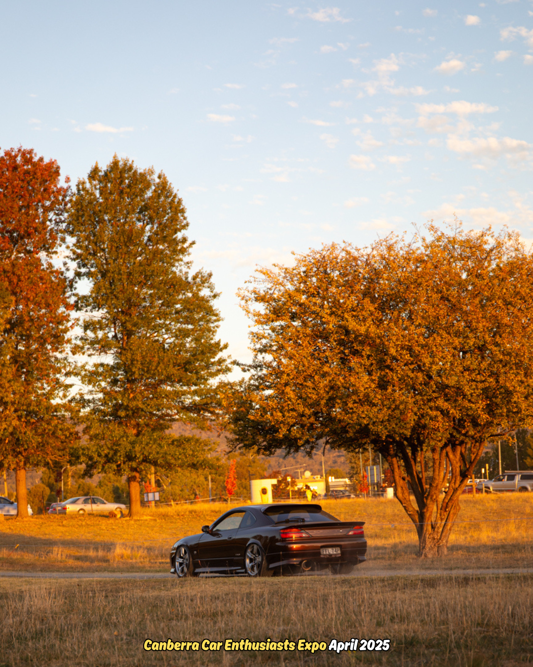 Black sports car parked on a dirt road near autumn trees during sunset.