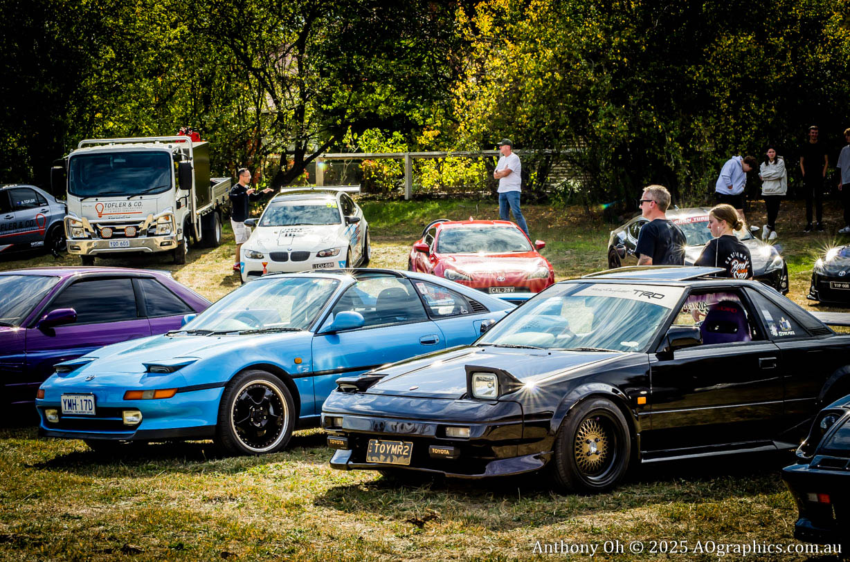 Classic sports cars, including a black Toyota MR2 and blue Nissan 180SX, parked at an outdoor car event.