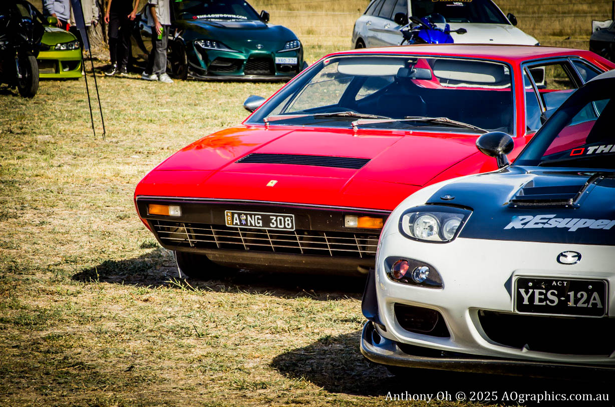 Front view of red Ferrari and white Mazda RX-7 parked on grass at car event.