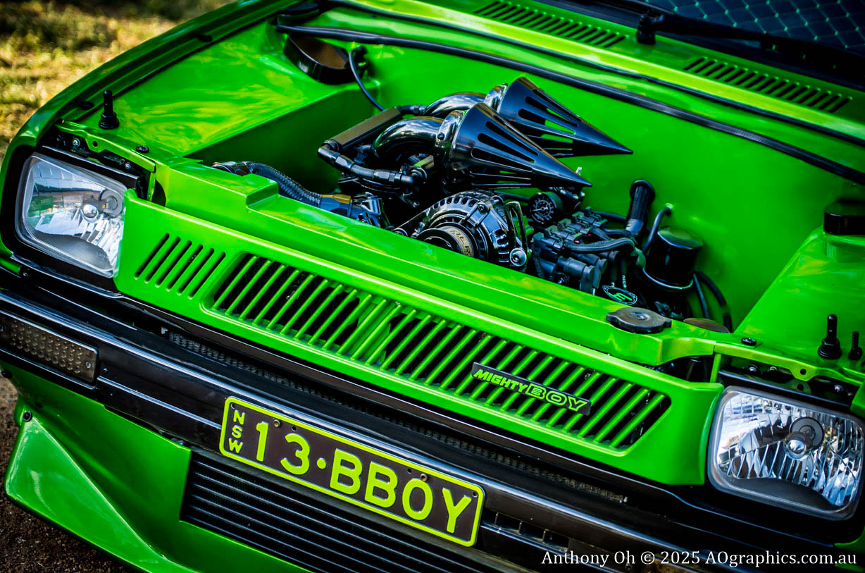 Bright green modified car engine with dual cone air filters and "Mighty Boy" badge.