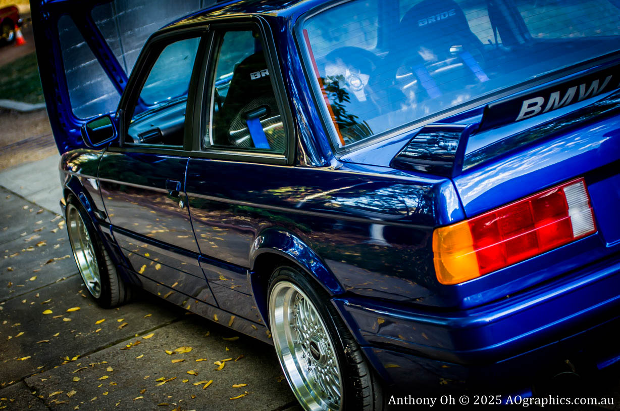 Blue BMW car with open hood, shiny chrome wheels, and clear taillights parked outdoors.