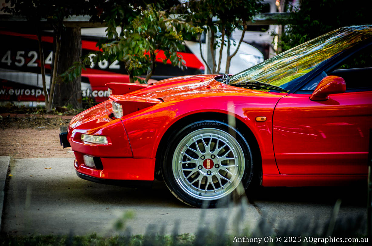 Close-up of a red sports car front with pop-up headlights and silver alloy wheels.