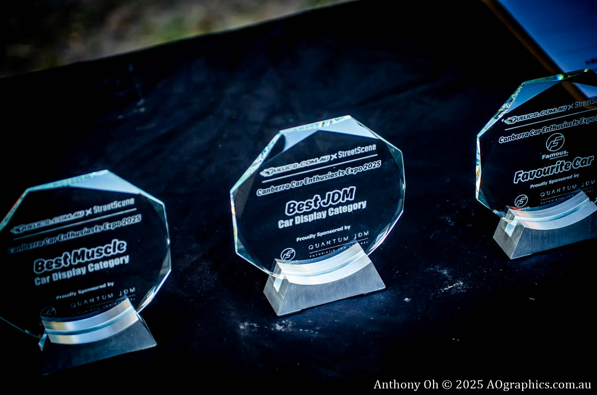 Three clear acrylic trophies on a black surface for car display categories at an expo.