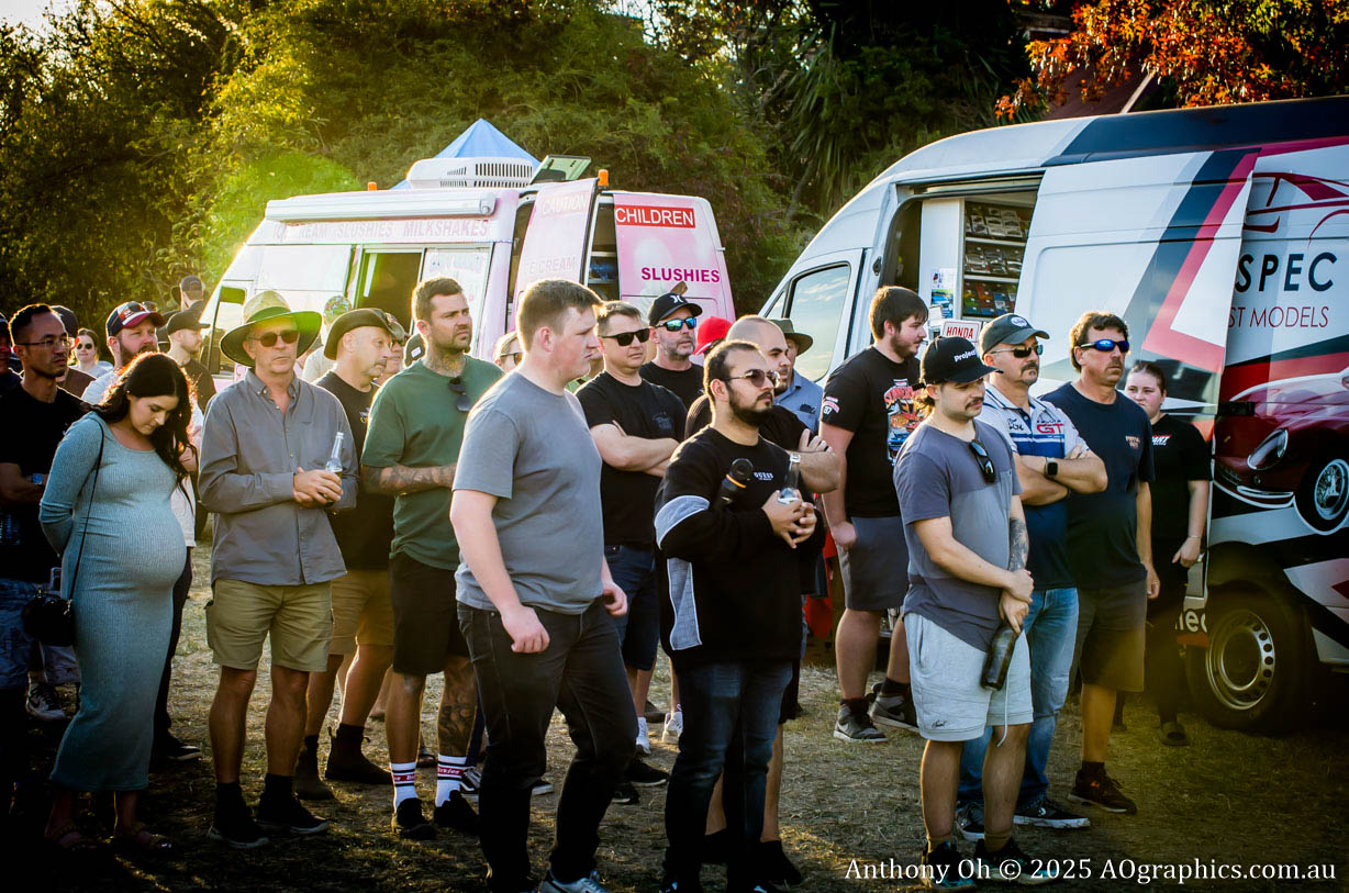 Group of people standing outdoors near food trucks in late afternoon sunlight.