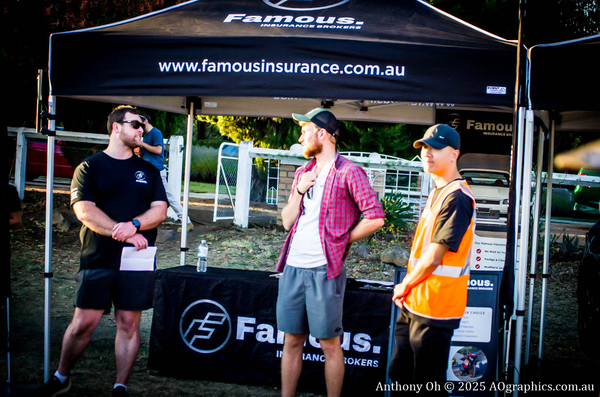 Three men standing and talking near a Famous Insurance tent at an outdoor event.