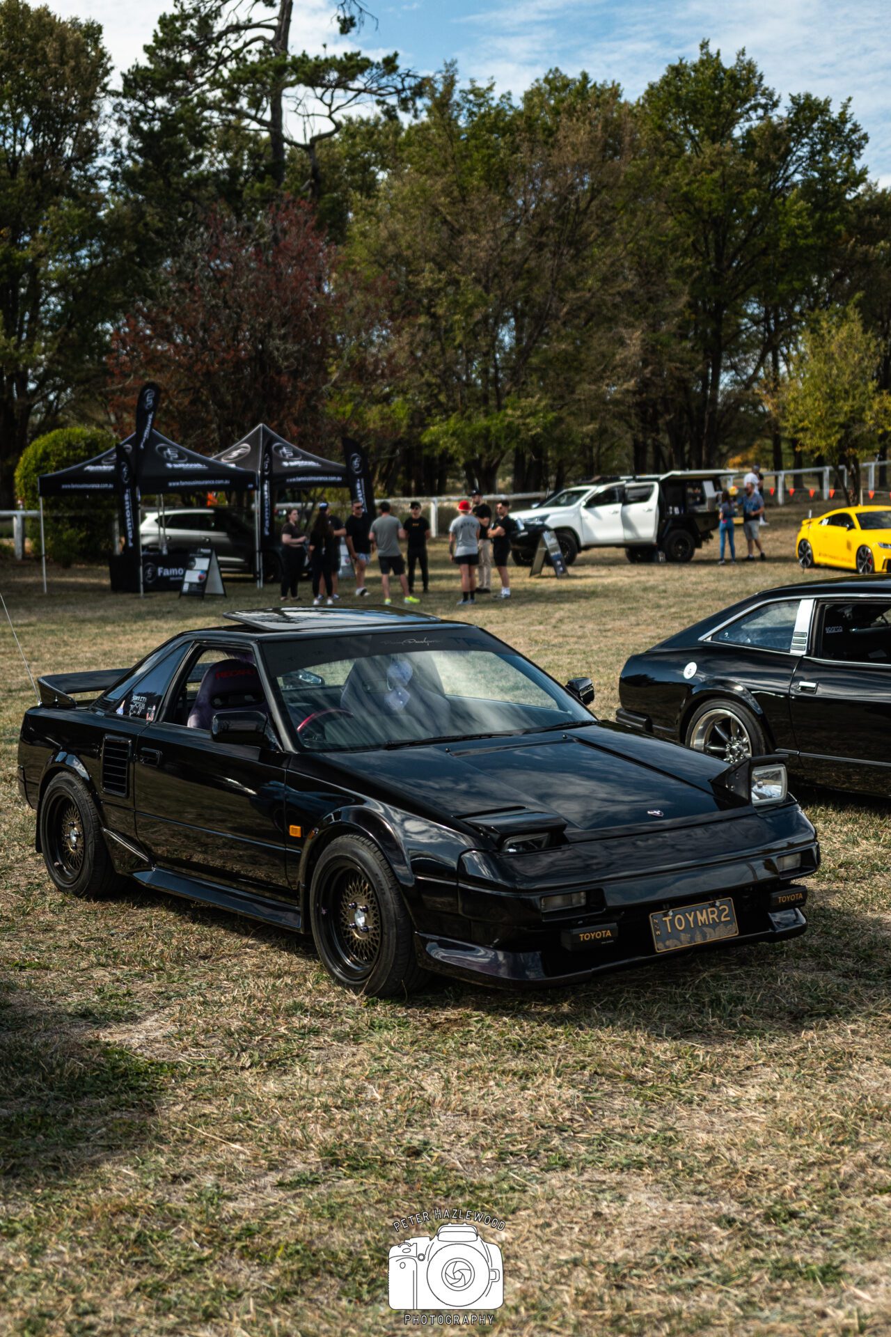 Black Toyota MR2 sports car parked on grass at an outdoor car event.