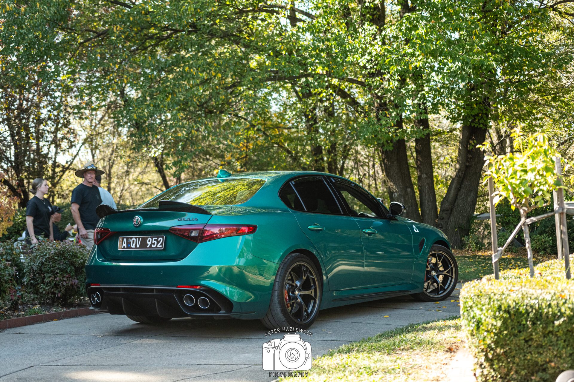 Green Alfa Romeo Giulia Quadrifoglio parked on a driveway with people and trees in the background.