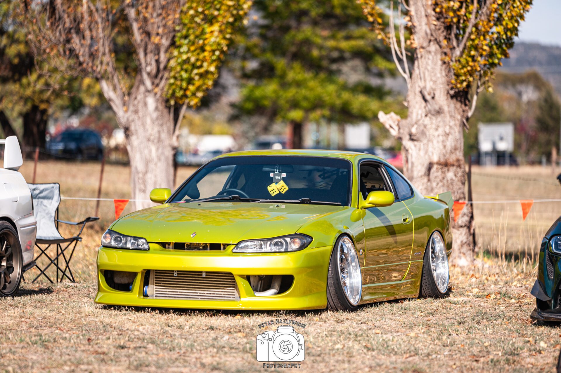Bright green modified sports car with wide chrome wheels parked on dry grass.