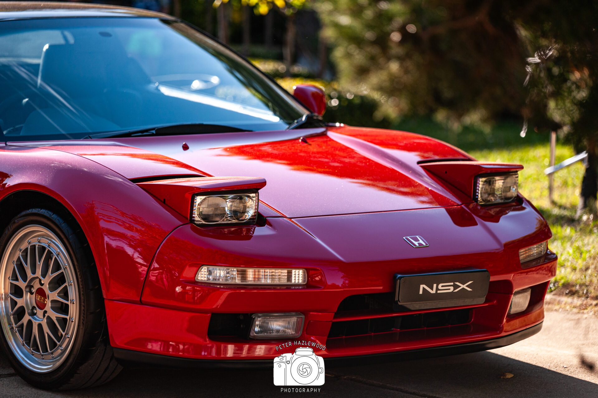 Close-up of a red Honda NSX sports car with pop-up headlights and alloy wheels in sunlight.