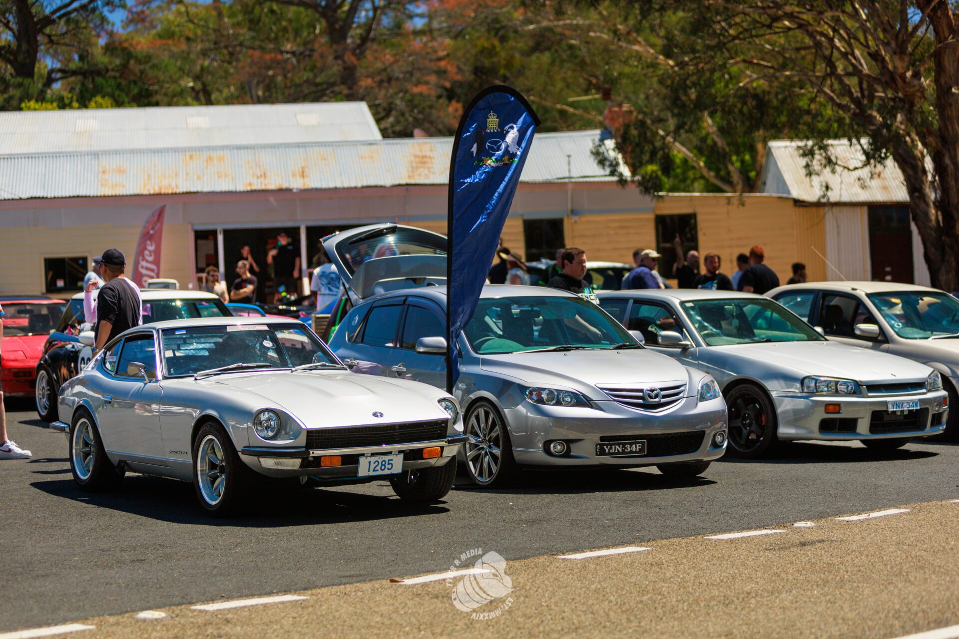 Three silver cars parked side by side at an outdoor car meet with people in the background.